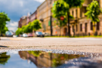 Sunny day after rain in the city, the empty road. Close up view from the level of the puddle on the pavement