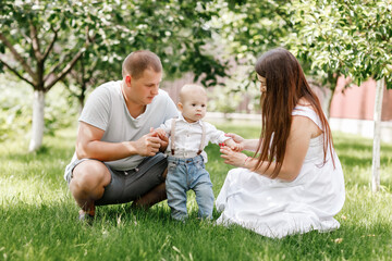 Naklejka na ściany i meble Happy young family, mom, dad and baby son spending time together outdoors in summer green garden