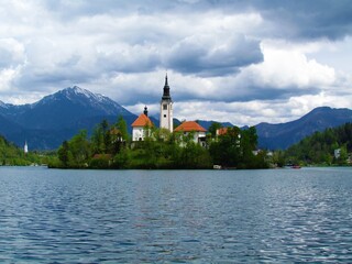 View of Bled lake and the island with the Pilgrimage church of the Assumption of Maria and Bled castle behind with snow covered peaks of Karavanke mountains