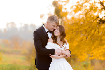 Front view of groom hugs the beautiful bride in the autumn park. Concept of newlyweds