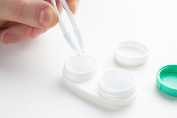 Hands picking up a contact lens with tweezers and maintenance material for contact lenses on white table. Eye health and care, eyesight and vision, ophthalmology and optometry concept.