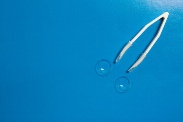 Tweezers and contact lenses. Blue background
