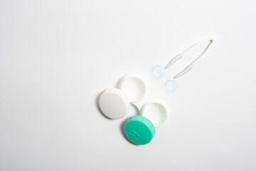 Contact lenses, tweezers and lens storage container on white background flat lay