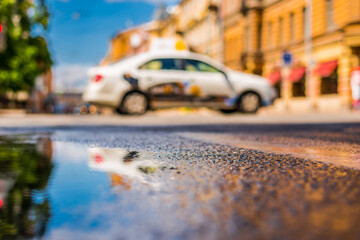 Sunny day after rain in the city, the car is driving across the road. Close up view from the level of the puddle on the pavement