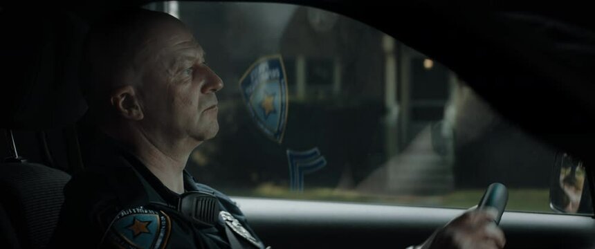 CU Caucasian American police officer patrolling streets of neighborhood in patrol vehicle. Shot with 2x anamorphic lens