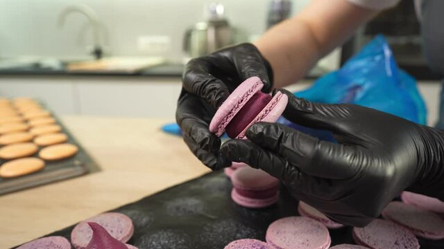 Process Of Making macaroon at home. Shot of hands of female pastry chef holding white macaron with ganache and squeezing red fruit jam from bag. Nature pastry macaroons. High quality 4k footage