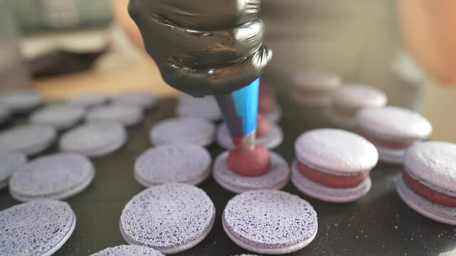 Process Of Making macaroon at home. Shot of hands of female pastry chef holding white macaron with ganache and squeezing red fruit jam from bag. Nature pastry macaroons. High quality 4k footage