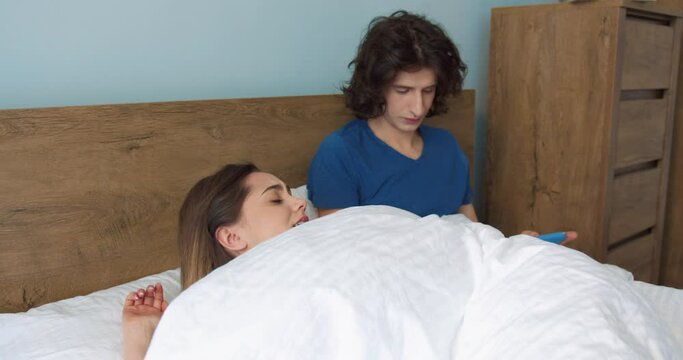 Don't bother me. Angry woman hiding under the blanket while her husband bothers her to sleep because using the tablet. Couple and morning concept