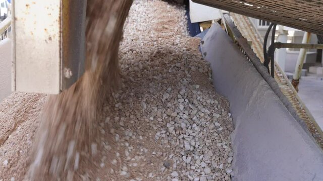 Close-up view of dry concrete pouring off a conveyor belt into a mixing car.