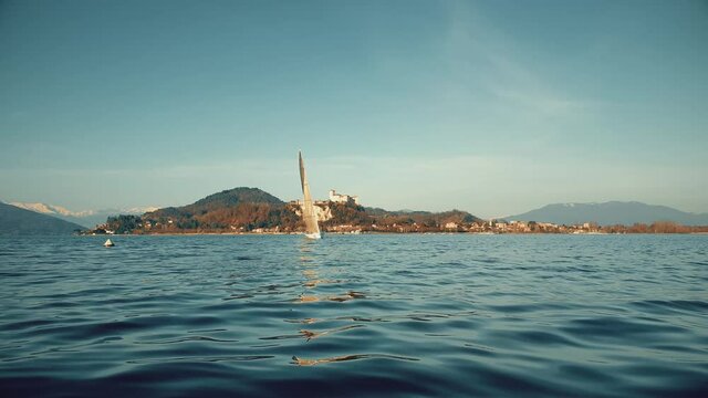 Low-angle pov of bow of boat sailing on Maggiore lake with castle in background. Italy