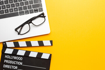 Office stuff with movie clapper, laptop, coffee cup, on yellow table - top view shot.