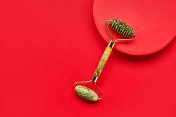 Green face roller from natural jade stone on a red background. SPA concept