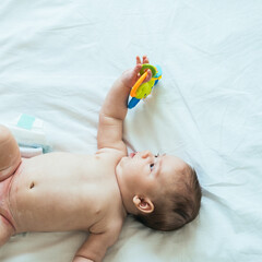 Cute Baby Holding Rattle Toy in Hand on White Sheets with Copy Space
Top view of naked infant with...