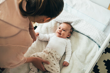 Mother putting her newborn baby to sleep at the crib.
High angle view of young mom bending forward...