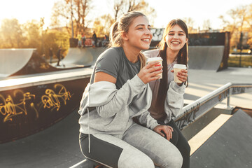 Two best female friends sitting at the skate park and joying in coffee to go.