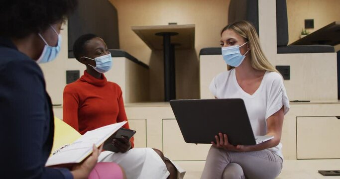 Three two diverse female office colleagues wearing face masks discussing together at office