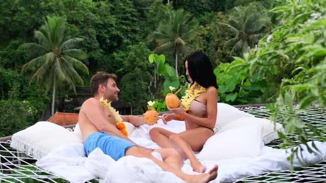 beautiful girl and man on a hammock in a Hawaiian flower necklace during her honeymoon, after the wedding, enjoying her vacation with her husband.Hawaiian girl showing leis flower necklaces