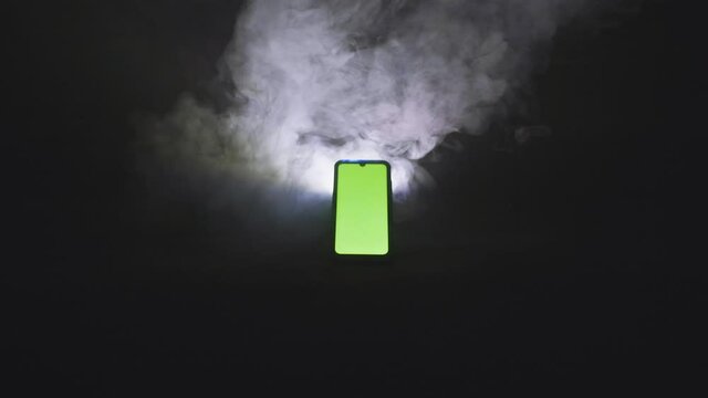 Smartphone avec fond vert sur fond isol&eacute; noir avec fum&eacute;e 