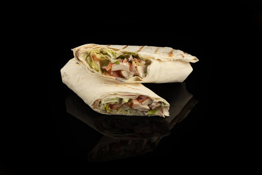 Classic shawarma kebab pita with chicken and vegetables and sauce on a black background. in section