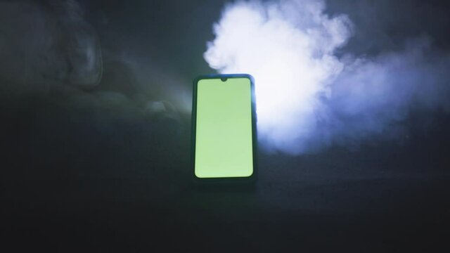 Smartphone avec fond vert sur fond isol&eacute; noir avec fum&eacute;e 