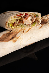 Classic shawarma kebab pita with chicken and vegetables and sauce on a black background. in section
