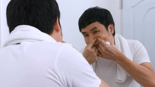 Man squeezing a pimple in the bathroom mirror