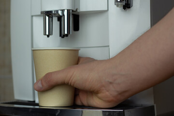 Closeup of a disposable coffee cup and coffee machine.