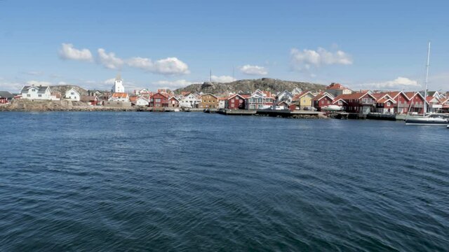 Old fishing village in the Swedish archipelago. A sailboat glides past. Old wooden houses can be seen in the background. Sunny day in the spring. Sk&auml;rhamn on Orust