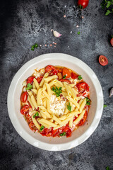 Baked feta pasta with cherry tomatoes, olive oil and herbs in a pan. Trend mixing macaroni and cheese. Food recipe vertical image, place for text, top view