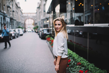 Fototapeta premium Young woman beside modern building on street in evening