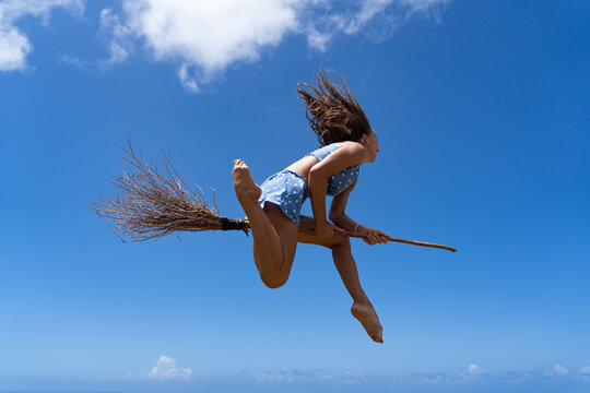 Young woman on the broom pretending to be witch on sky background