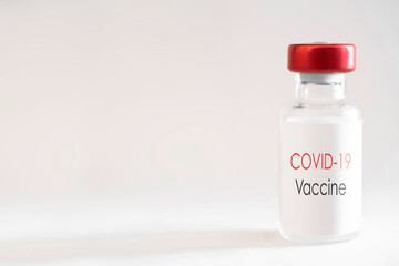 Vaccine bottle with red cap and the English text 'Covid-19 Vaccine' on a white background with shadow. Liquid for injection. Shallow depth of field. Copy space