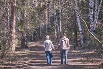 Elderly interracial couple walking in a spring forest park holding hands.