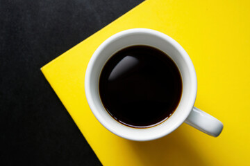 Top view a cup of black coffee on yellow paper and black table background.   