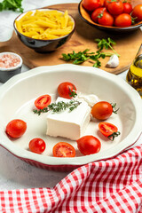 Preparation of ingredients for trending feta pasta with cherry tomatoes herbs and garlic, vertical image, top view