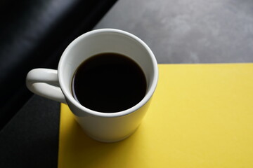 A cup of black coffee on yellow paper and loft style table and part of sofa background.
