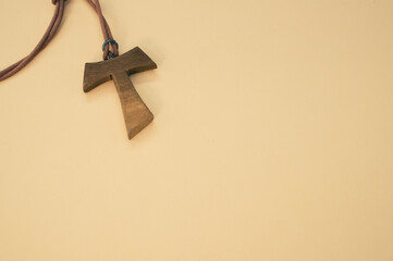 Closeup shot of a wooden tau cross necklace isolated on a brown background - obrazy, fototapety, plakaty