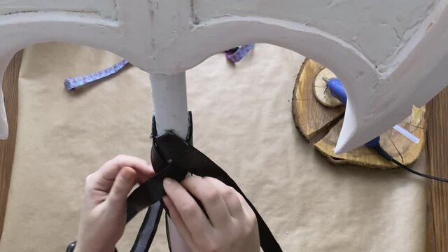 Girl weaves crosswise leather ribbons on handle of hatchet. Woman makes viking axe for cosplay festival. DIY Celtic weapons in craft workshop.