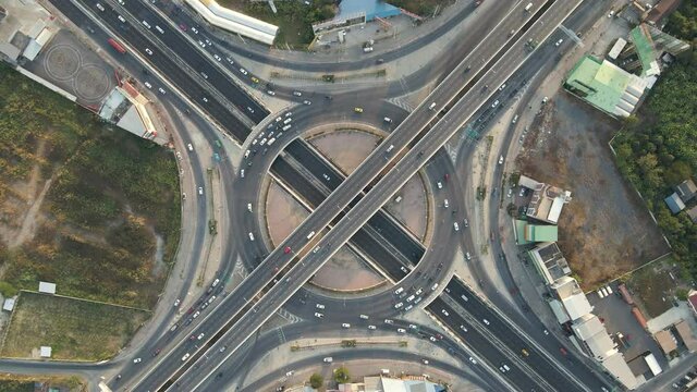 Top-down zoom in aerial drone shot of roundabout and x-shaped crossing expressway with evening busy traffic.