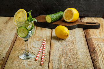 Cocktail cucumber water with lemon and mint in a glass on a wooden table on a black background near lemon and cucumber.