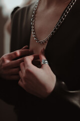 Female hands touching silver chain hanging around the neck of a woman dressed in a black jacket....