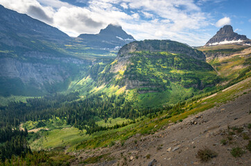 Morning sun lits up the Heavy Runner Mountain and surrounding peaks along the Going To The Sun Road in Glacier National Park, Montana, USA. Green valley in Rockies in a soft haze on a sunny day.