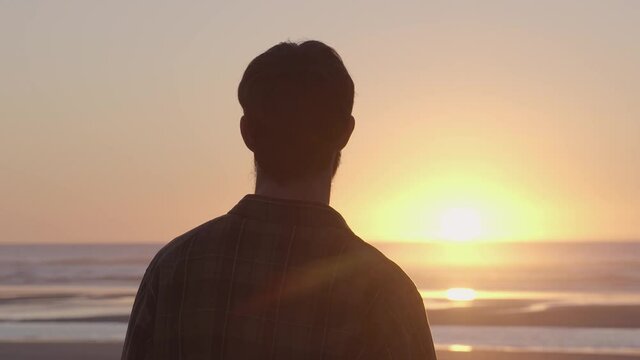Young unrecognisable man contemplating a beautiful sunset by the sea: Freedom in a lonely beach