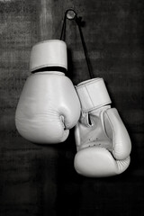 White leather boxing gloves hanging on black wall