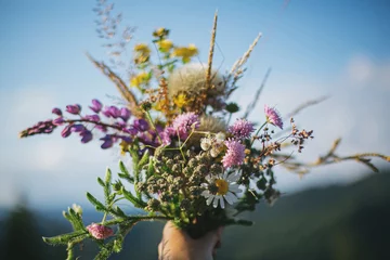 Foto op Aluminium Beautiful colorful bouquet of wildflowers in hand on background of mountain hills and sunny sky © sonyachny