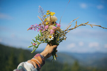 Beautiful colorful bouquet of wildflowers in hand on background of mountain hills and sunny sky © sonyachny