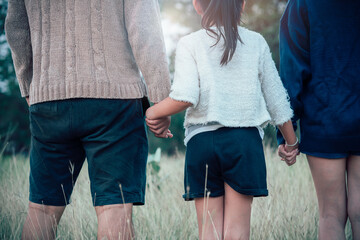 Straight black haired girl holding her mother and father hands walking outdoors in park