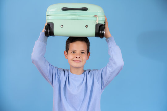 Happy young boy with a suitcase over his head over blue background