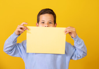 Smiling boy portrait holding blank paper. Isolated on yellow background