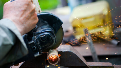 The worker cuts metal, steel with a grinder. the pipe is clamped in a vice, sparks fly. close-up, the hands of a man using a grinder to cut a pipe, bright flashes flying in different directions.